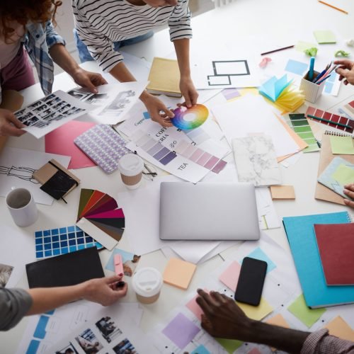 High angle close up of creative business team working on design project focus on table with photographs and color swatches scattered around, copy space