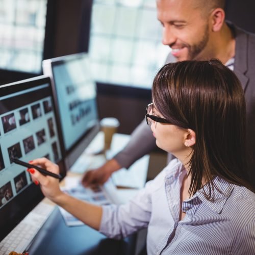 Female photo editor discussing over computer with male colleague in creative office